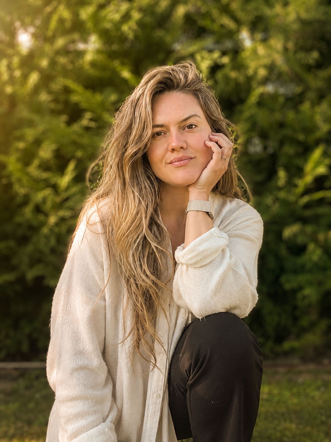 Naianna Robertsson seated outdoors in a cream knit jumper, surrounded by greenery