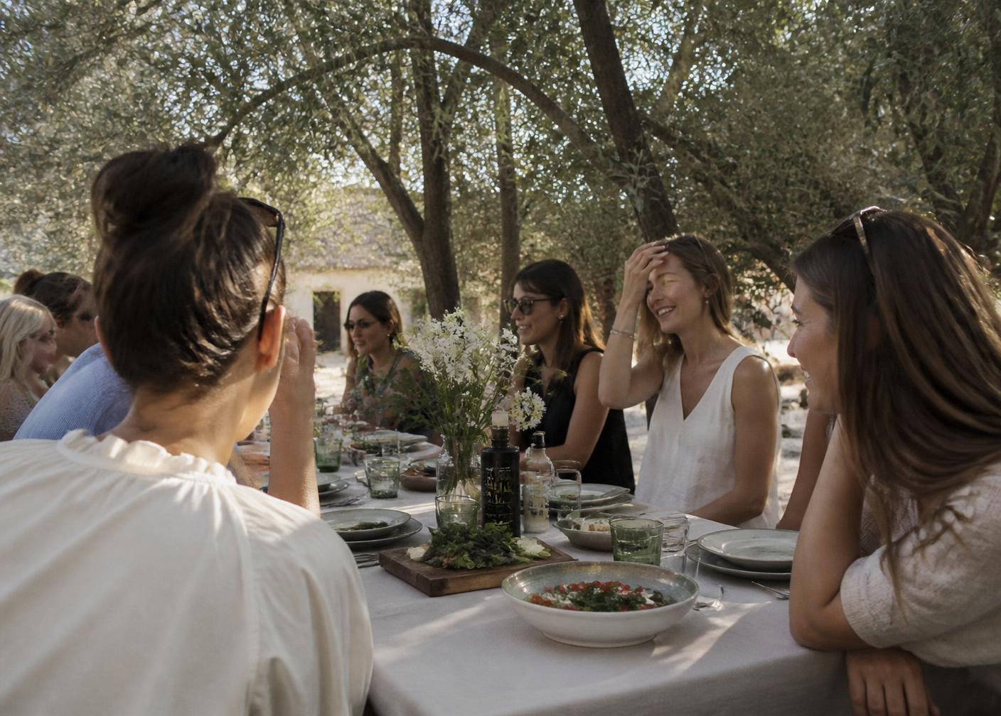 Women gathered around a long wooden table outdoors in summer light